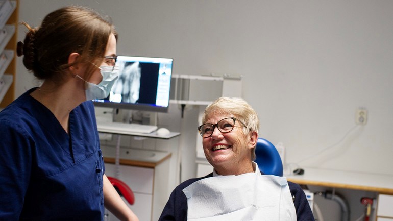 Äldre patient i tandläkarstol ler mot tandvårspersonal.